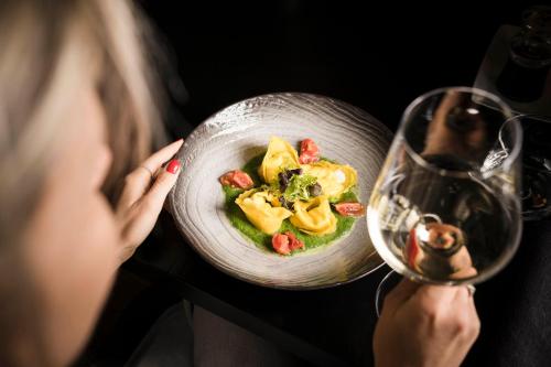a woman looking at a bowl of food and a wine glass at Alpine Boutique Villa Gabriela - Adults Only in Castelrotto