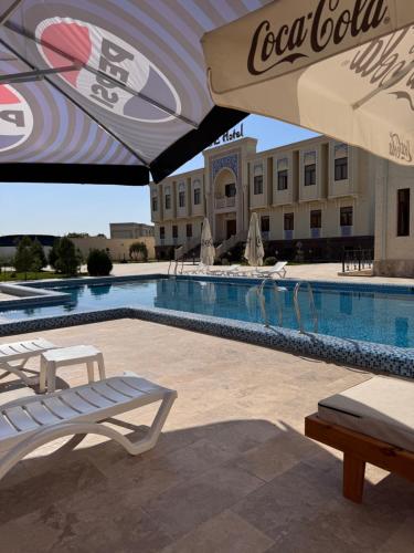 Una piscina con sillas y sombrilla al lado de un hotel. en Hotel Ark Premium, en Bukhara