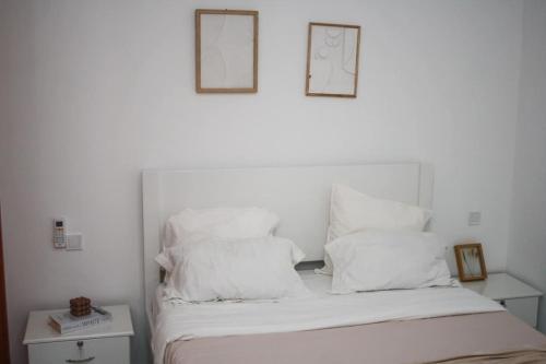 een bed met witte kussens en twee foto's aan de muur bij Apartment Morabeza in Praia Cidadela in Praia