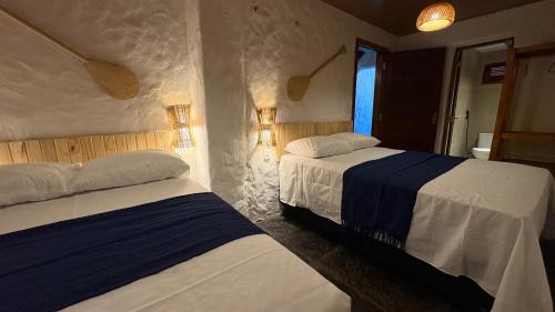 two beds in a bedroom with two lamps on the wall at Casa Monan, Atins beach in Atins