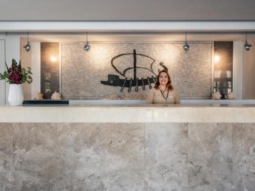 a woman standing behind a counter in a lobby at Pedi Beach Hotel in Symi