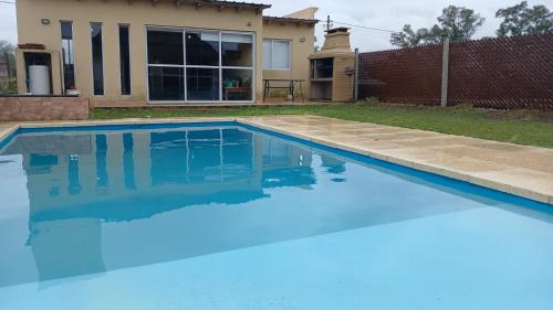 a blue swimming pool in front of a house at Casa 3 dormitorios en Barrio Privado con vigilancia en Haras el Terraplen, General Rodriguez, con Pileta, quincho, parrilla in General Rodríguez