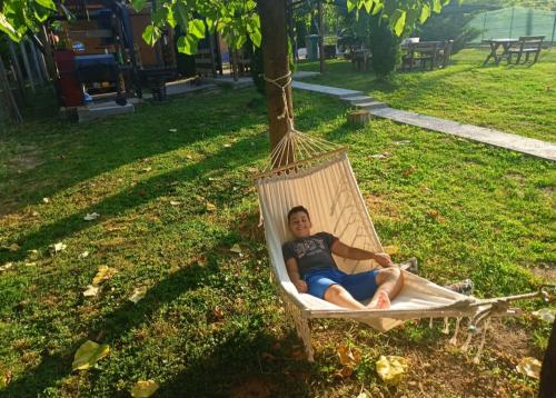 a man sitting in a hammock under a tree at Eko dan in Železnička Stanica Karlovački Vinogradi