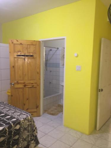 ein Schlafzimmer mit gelber Wand und ein Badezimmer mit Dusche in der Unterkunft Cozy Oasis Hideaway in Port Antonio