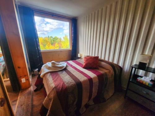 a bedroom with a bed with a blanket and a window at La Maison Conteneur in Amos
