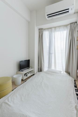 a white bedroom with a bed and a window at Yakuin apartment in Fukuoka