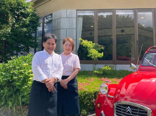 a man and a woman standing next to a red car at Forest Villa YUMESUZU the Closest Accommodation to the Metasequoia Tree-lined Avenue in Takashima