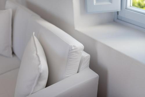 a white couch with two pillows next to a window at Aria Suites & Villas in Fira