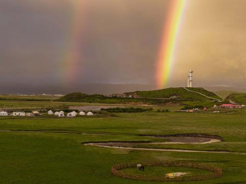 Un arcoíris sobre un campo de golf con un faro. en Hongyuan Weilu Nomadic Luxury Camp, en Hongyuan