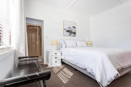 a white bedroom with a bed and a chair at Matahari Apartments and Villas in Upper Hutt