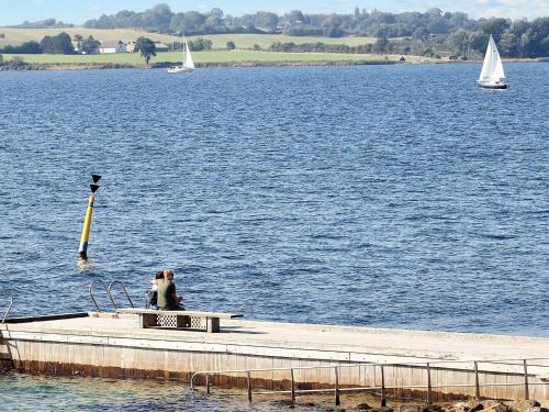 two people sitting on a dock on a lake with sailboats at Faaborg Holiday Centre in Fåborg