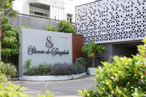 a sign in front of a building with purple flowers at Shewin de Bangkok in Ban Bang Bamru