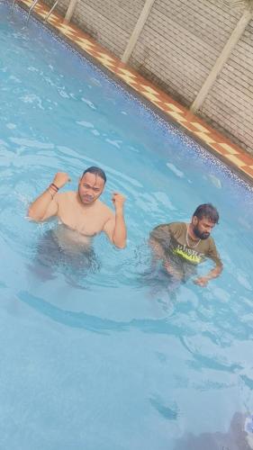 two men are swimming in a swimming pool at Tripathi Villa in Murbād