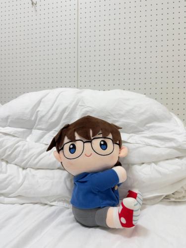 a doll with glasses sitting on a bed at D Regalo in Ichikawa