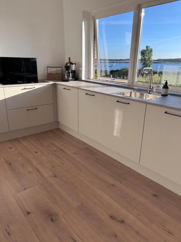 a kitchen with white cabinets and a large window at Udsigtsvilla Tambohus in Thyholm