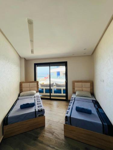 two beds in a room with a large window at Mehdia's Paradise in Kenitra