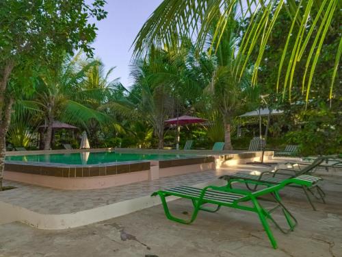 a swimming pool with two green chairs and trees at Escape Hole in Diani Beach