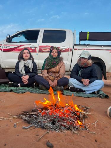 three people sitting around a fire in front of a truck at Catalina Luxury rum camp in Wadi Rum