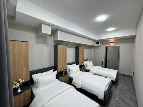 タシュケントにあるArt City Hostelの白いシーツが敷かれたベッドが3つあるホテルの部屋