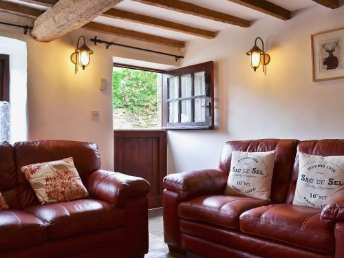 a living room with two leather couches and a window at Post Office Cottage in Highpeak Junction