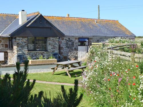 Una cabaña de piedra con mesa de picnic y flores. en The Old Stable, en Holywell Bay
