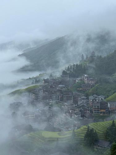 a small town on a hill in the fog at Longsheng Longji Rice Terraces Jingyue Hotel 龙胜龙脊梯田境悦酒店 in Longsheng
