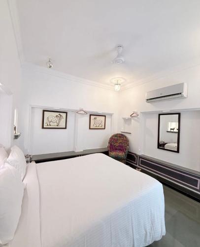 a white bedroom with a large white bed and a fan at Little Garden Guest House in Udaipur