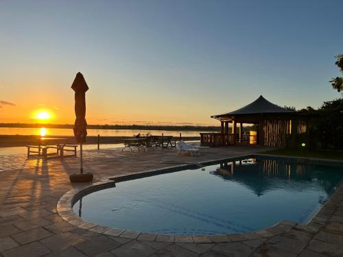 a swimming pool with a gazebo and a sunset at Breezes River Lodge in Chirundu