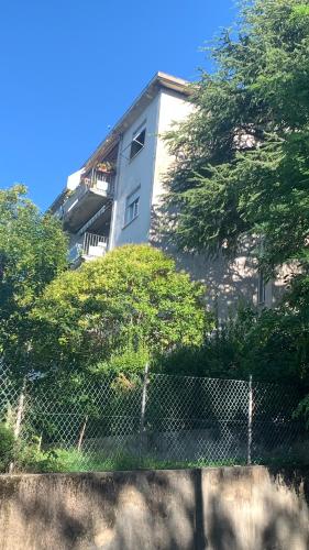 a building with a fence and trees in front of it at Affittacamere via Moncolano mare Barcola in Trieste