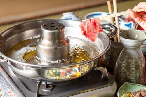 a person cooking food in a pan on a stove at Yaki no Yu - Vacation STAY 29804v in Takayama
