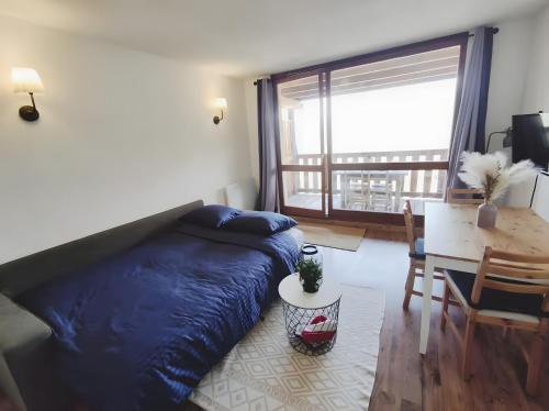 1 dormitorio con cama azul, mesa y ventana en Studio au coeur de Praloup, en Pra-Loup