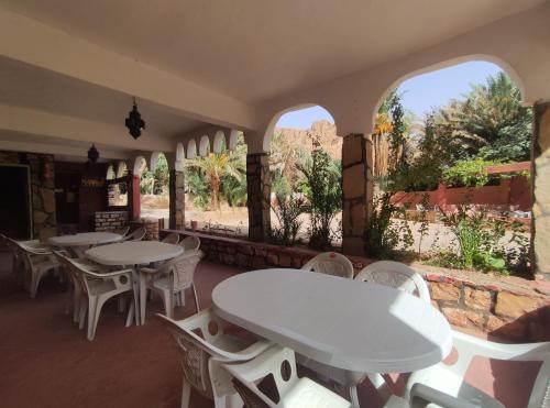 a restaurant with white tables and chairs and windows at Le LAC Auberge Camping Todra in Tinerhir