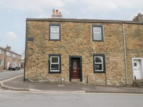 a brick building with a red door on a street at Cosy Cottage in Cumbria, West of Lake District in Broughton Moor