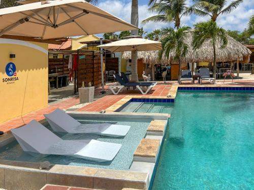 a swimming pool with two chairs and umbrellas at Sonrisa Boutique Hotel - Adults Only in Kralendijk