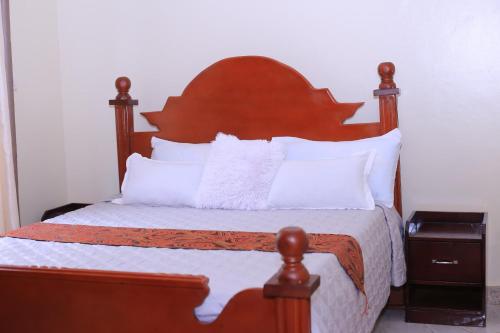 a bed with a wooden head board and white pillows at Tasha's suites in Entebbe