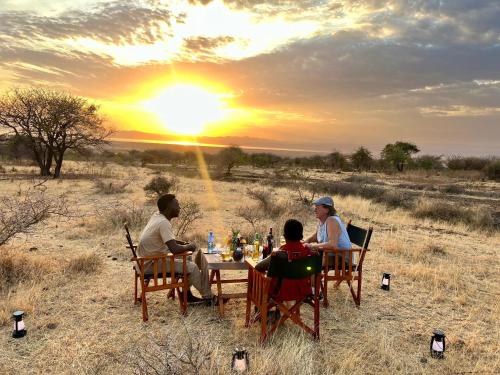 a group of three people sitting at a table with the sunset at Furaha Luxury Lodge in Mto wa Mbu