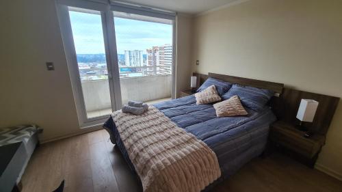 a bedroom with a blue bed with a large window at Departamento Estudio Central in Temuco