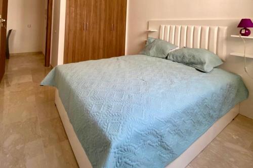 a bedroom with a bed with a blue comforter and pillows at Appartement Moderne et Équipé Proche Aéroport CMN in Nouaseur