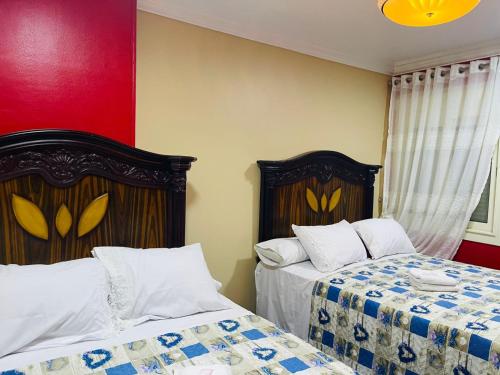 a bedroom with two beds and a red wall at B&KHOME Banha in Banī Ghālib