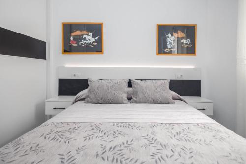 a bedroom with a white bed with two pictures on the wall at Apartamentos L O L A Arguineguin in Arguineguín