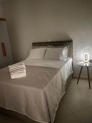 - un lit avec des draps et des oreillers blancs ainsi qu'une table de nuit dans l'établissement Lar Urbano, à Manhuaçu