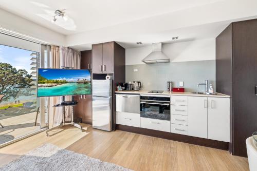 a kitchen with white cabinets and a tv on the wall at Paihia Beachfront 1 Bedroom Aptm in Paihia