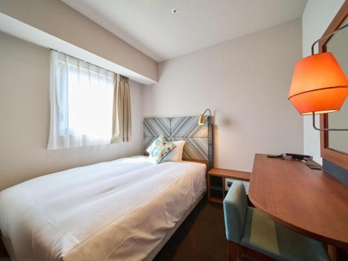 a bedroom with a bed and a desk and a window at Meitetsu Inn Nagoya Kanayama Annex in Nagoya