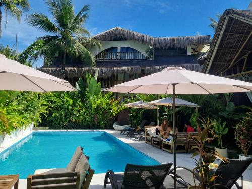 Una piscina de resort con sombrillas y gente sentada. en Villa Cali Siargao, en General Luna