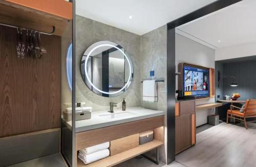 a bathroom with a sink and a mirror and a television at Shantou New Town Huanghe Road Yifei Hotel in Xialian