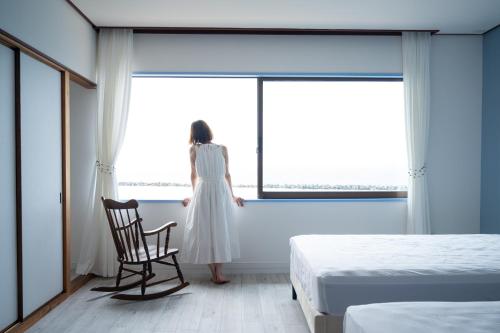 a woman in a white dress standing in a bedroom looking out the window at DAISEN UMIHOTARU Entire house in Daisen