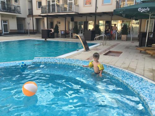 un petit garçon dans une piscine avec un ballon dans l'établissement Palvile Apartmani, à Palić
