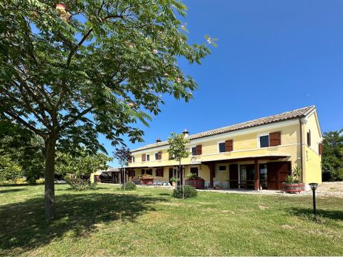 a large yellow building with a tree in the yard at Casale Casini Soccorso, residenza di campagna in Senigallia