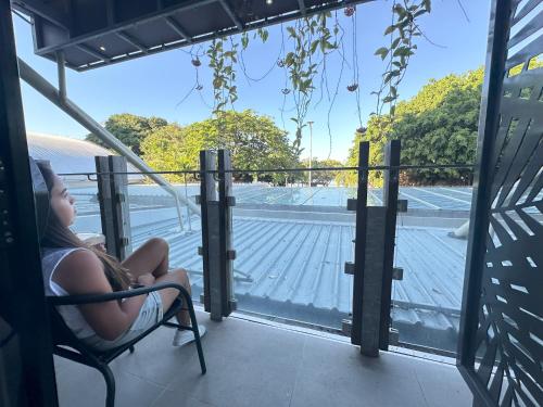 a woman sitting in a chair on a balcony looking at a tennis court at Global Backpackers Cairns in Cairns