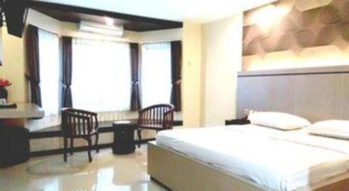 a bedroom with a bed and two chairs and windows at Alexander Hotel Tegal in Tegal